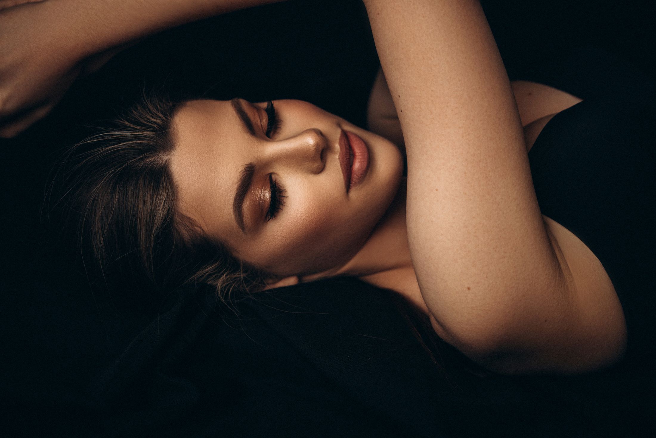 Woman with closed eyes, resting against dark background.