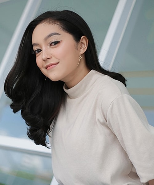 Smiling person with long, dark hair indoors.